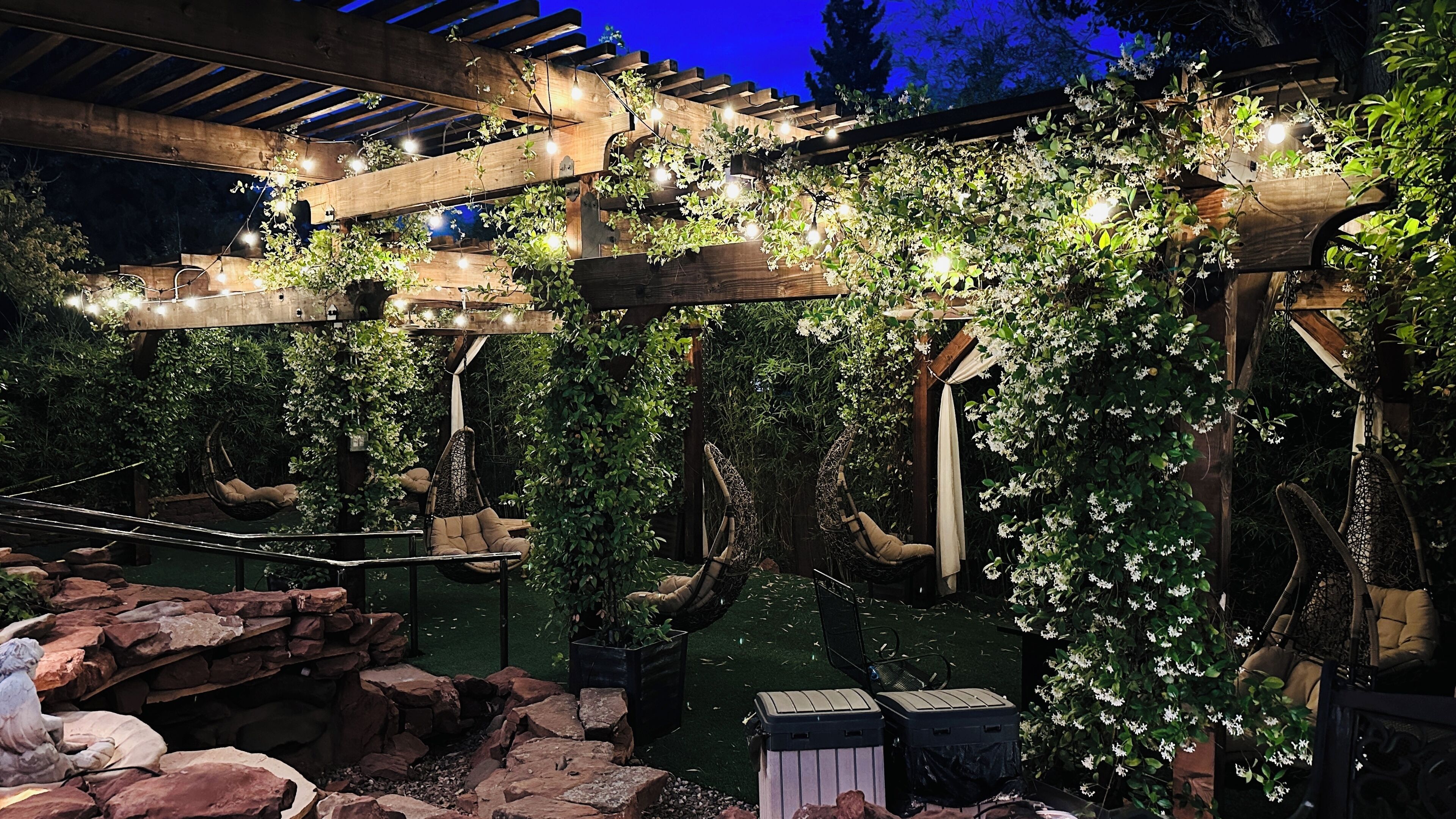 Une terrasse de jardin agrémentée de pergolas en bois, de fauteuils suspendus et de guirlandes lumineuses.