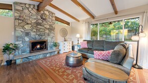 A cozy living room with a stone fireplace, wooden beams, a large window, and a comfortable seating area.