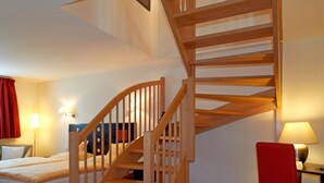 A hotel room with a wooden staircase, a bed, a desk, and a chair. - Hôtel Chez Jean (Saverne)