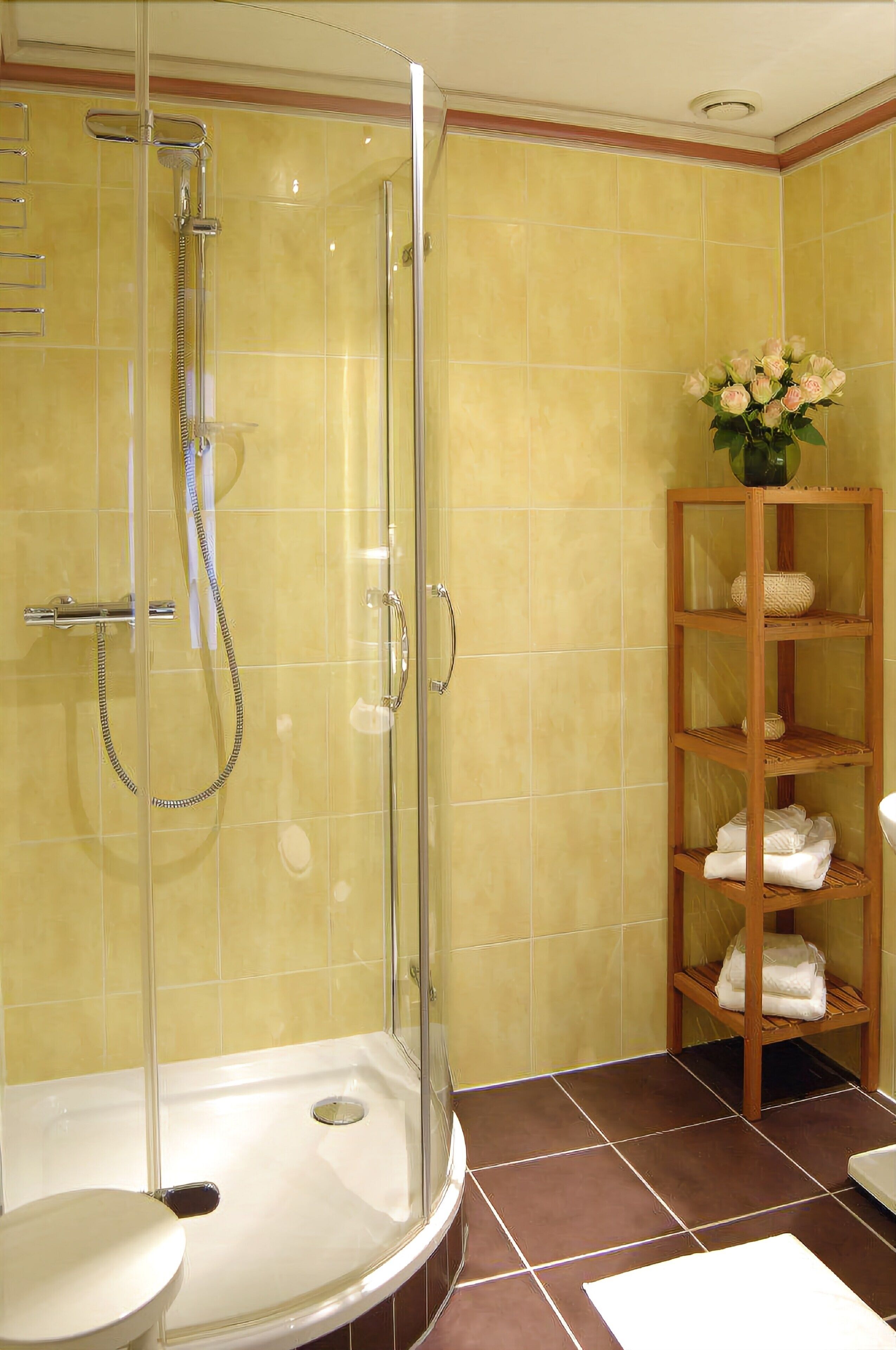 Un baño con ducha de vidrio, inodoro y estante de madera con toallas.