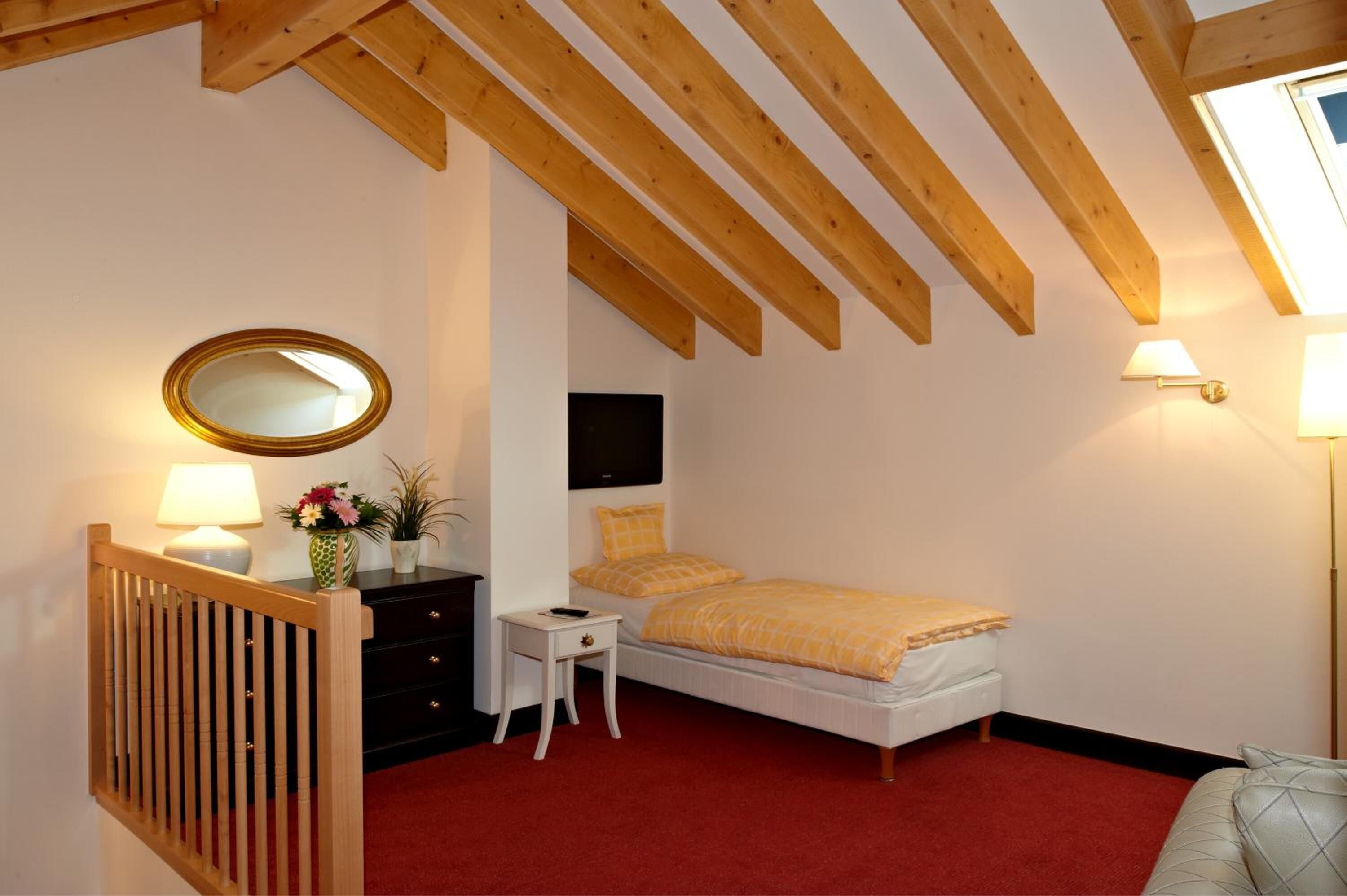 Un dormitorio con cama, cómoda, espejo, mesita de noche con lámpara y ventana con vistas.