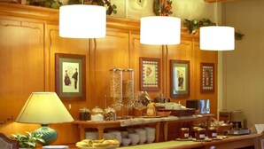 A buffet setup with various food items and condiments, a lamp, and framed pictures on the wall. - Hôtel Chez Jean (Saverne)