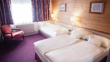 A hotel room with two beds, a red chair, a radiator, and two wall-mounted lamps.