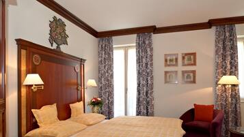 A hotel room with a large bed, two bedside lamps, a wooden headboard, a red armchair, and a window with curtains.