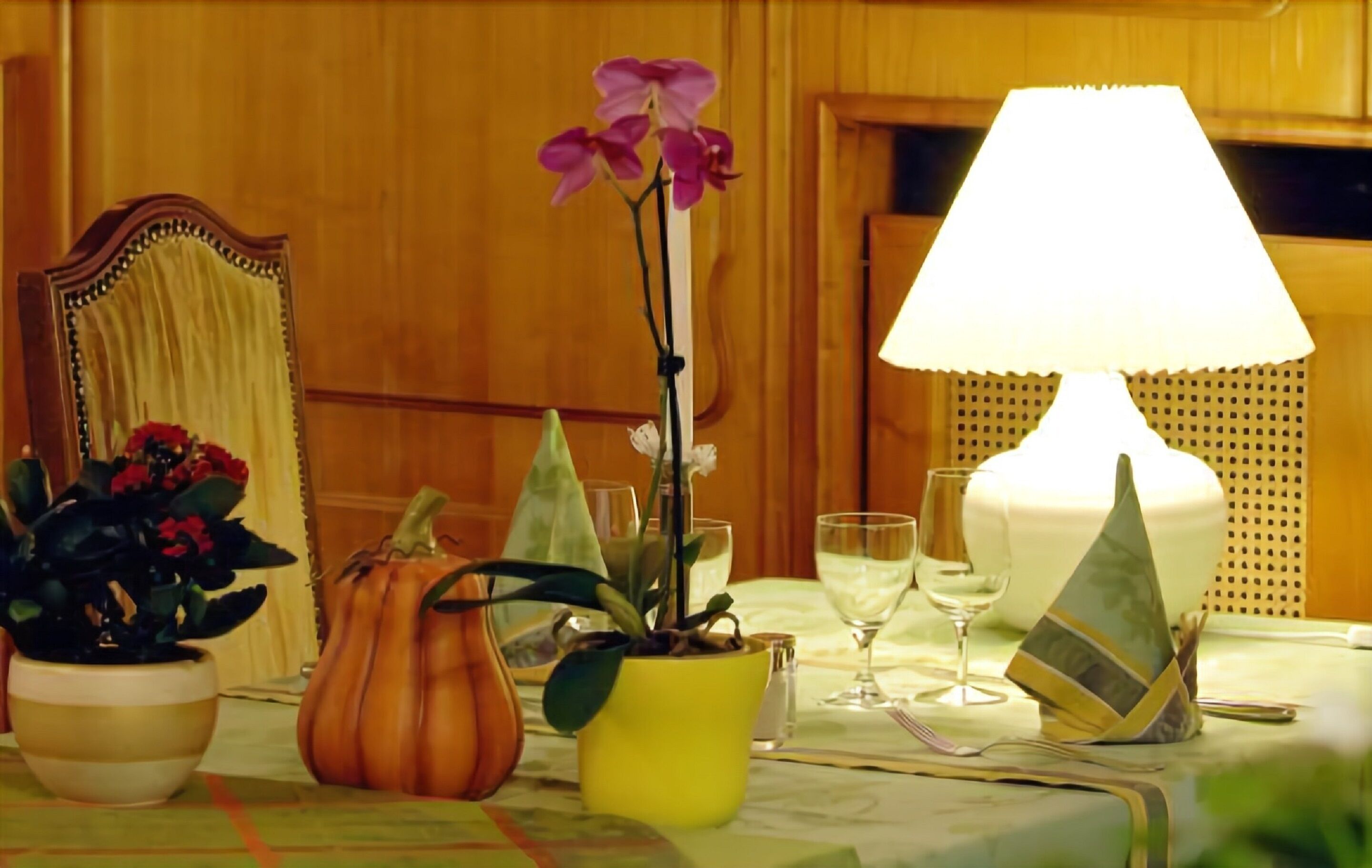 A table set with a lamp, wine glasses, and potted plants.