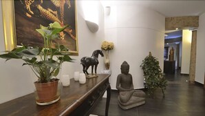 A serene lobby with a wooden reception desk, a large leopard painting, a statue of a horse, a Buddha statue, and a potted plant. - Hôtel Chez Jean (Saverne)
