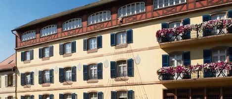Un edificio de varios pisos con un estilo arquitectónico tradicional europeo, que cuenta con un restaurante en la planta baja y un letrero visible que dice 'Chez Jean'.
