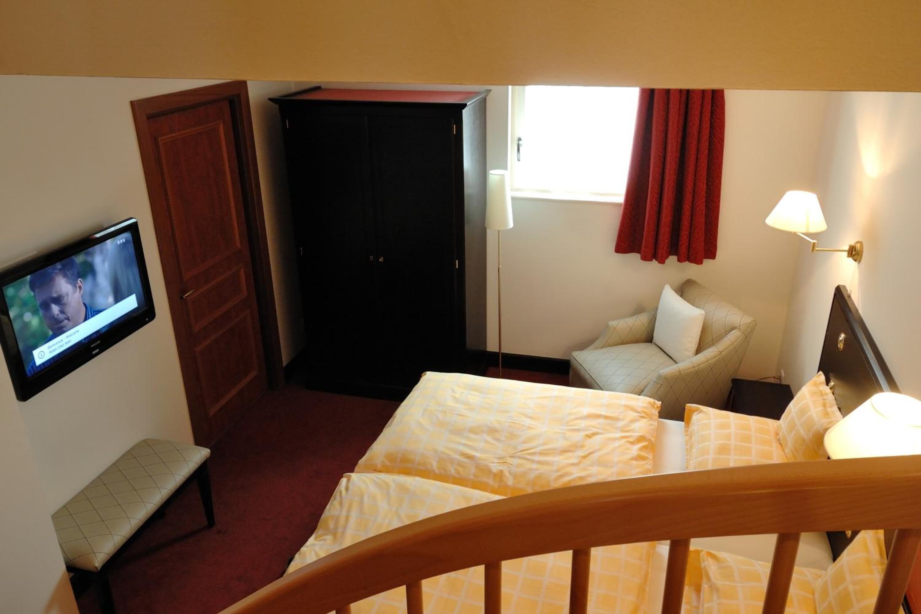 Een hotelkamer met een bed, een bankje, een televisie, een kast en een raam met gordijnen.