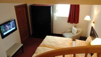 Een hotelkamer met een bed, een bankje, een televisie, een kast en een raam met gordijnen.