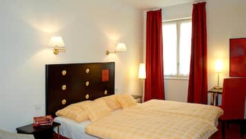 Une chambre d’hôtel avec un grand lit, deux lampes de chevet, une table de chevet, un fauteuil rouge et une fenêtre avec des rideaux rouges.