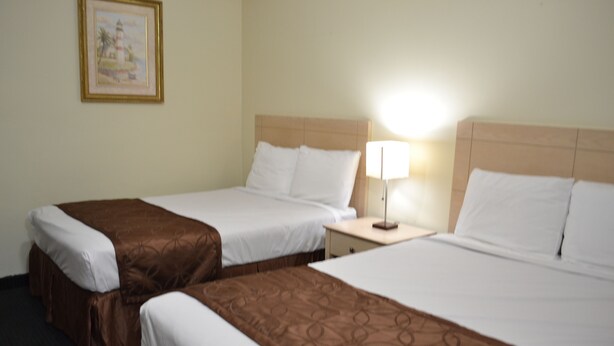 A hotel room with two beds, a nightstand, a lamp, and a framed picture on the wall.