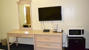 A room with a wooden desk, a flat-screen TV, a coffee maker, and a microwave.