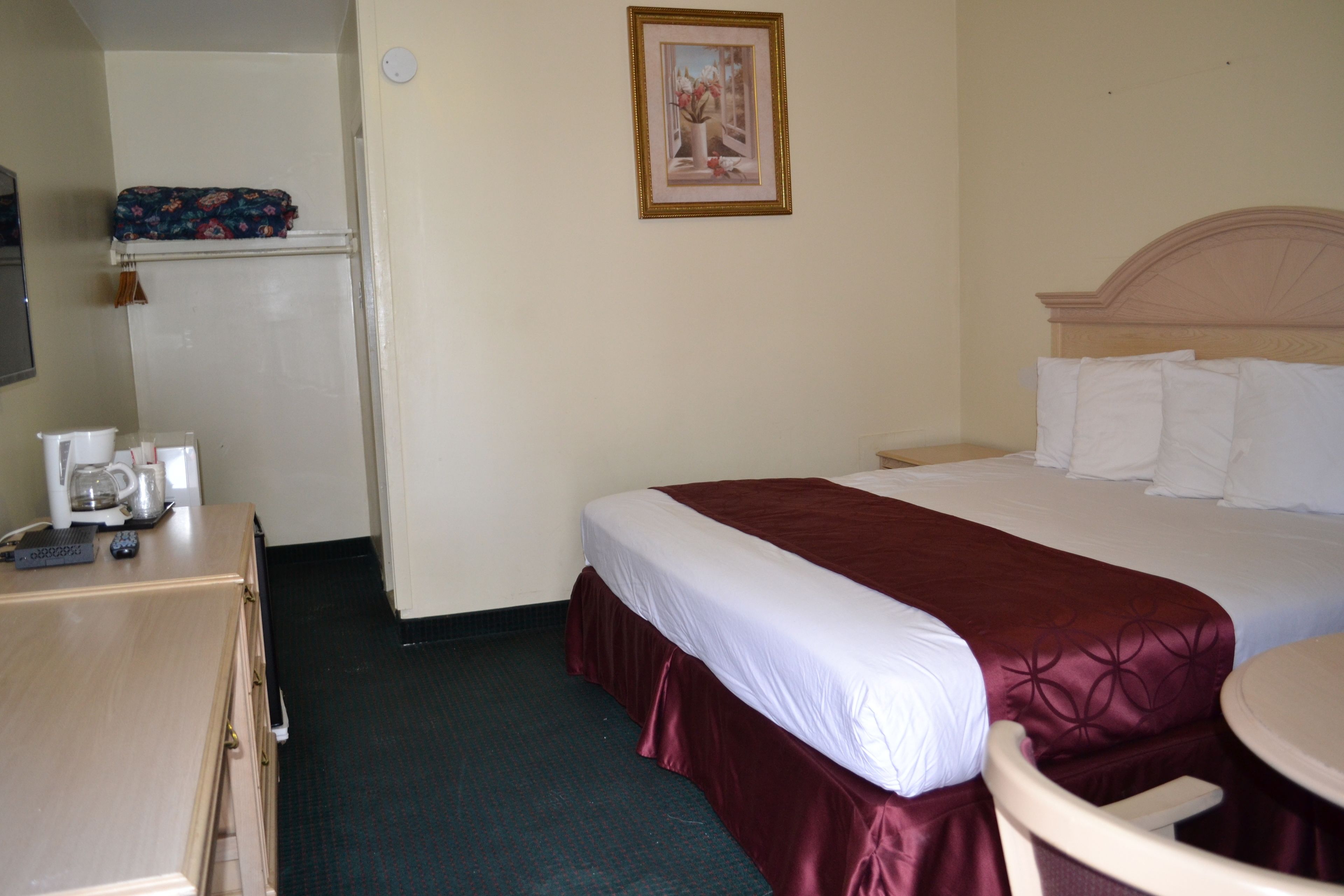 A hotel room with a bed, a desk with a telephone and a coffee maker, a small table, and a picture on the wall.