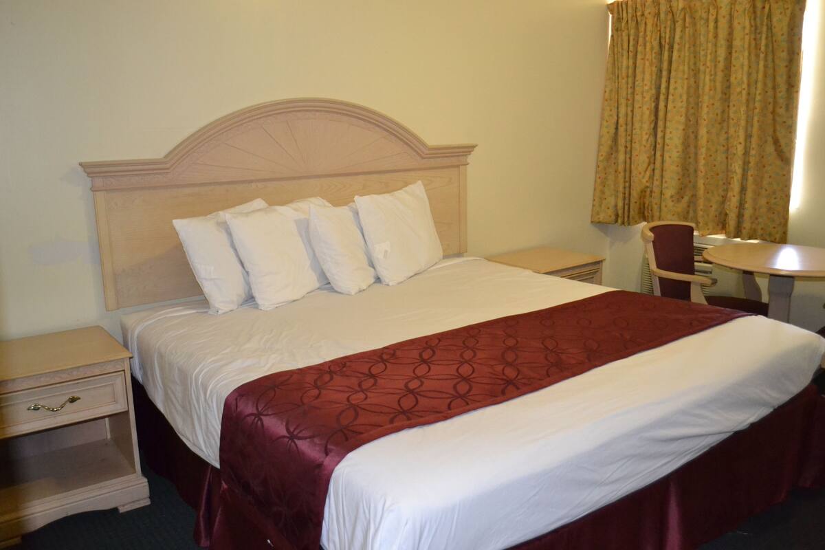 A hotel room with a bed, a nightstand, a chair, and a small table.