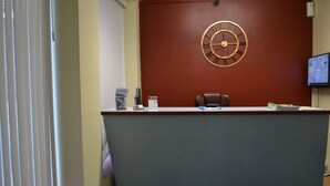 A reception desk with a clock, a television screen, and a chair.