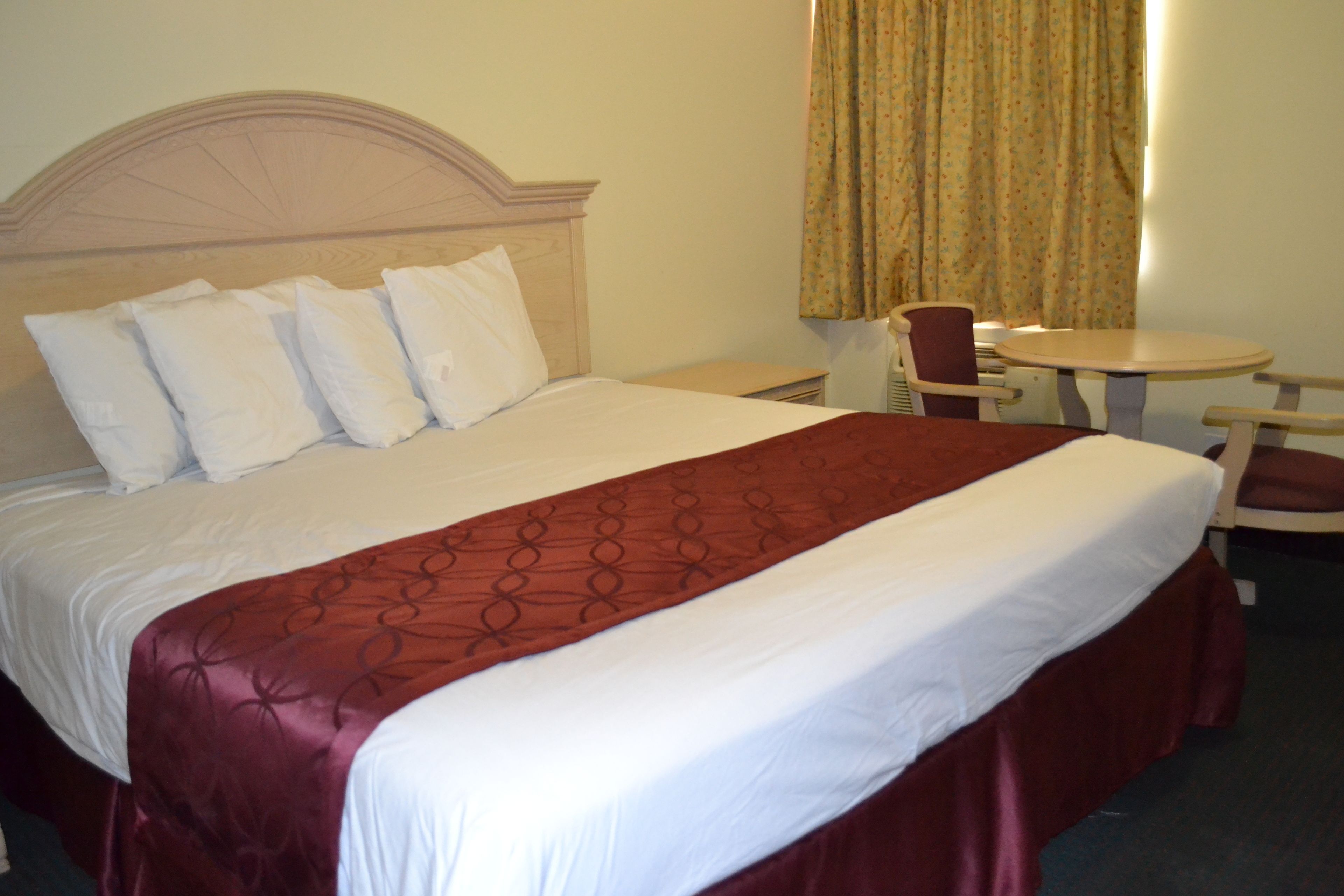 A hotel room with a large bed, a wooden headboard, a small table, and a chair.