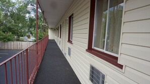 A covered outdoor corridor with a red railing, beige siding, and windows with red trim.