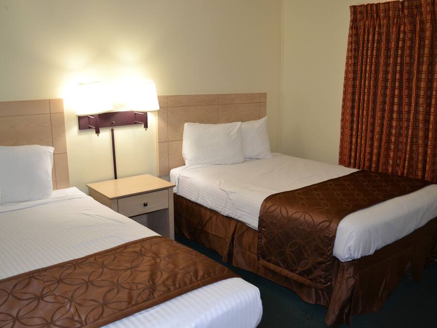 Una habitación de hotel con dos camas, una mesita de noche, una lámpara y una cortina.