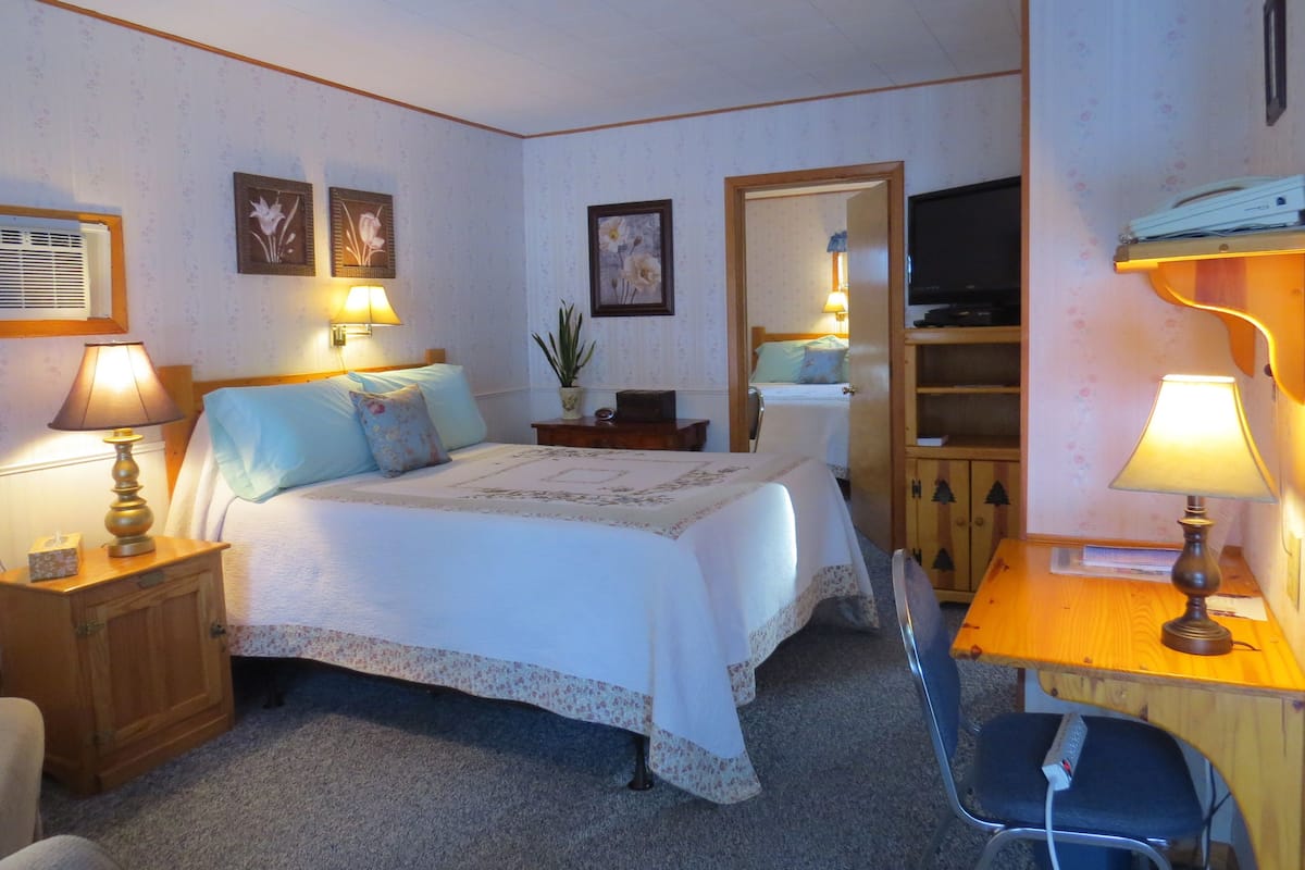 A bedroom with a bed, bedside tables, a desk, a chair, a television, and a mirror.