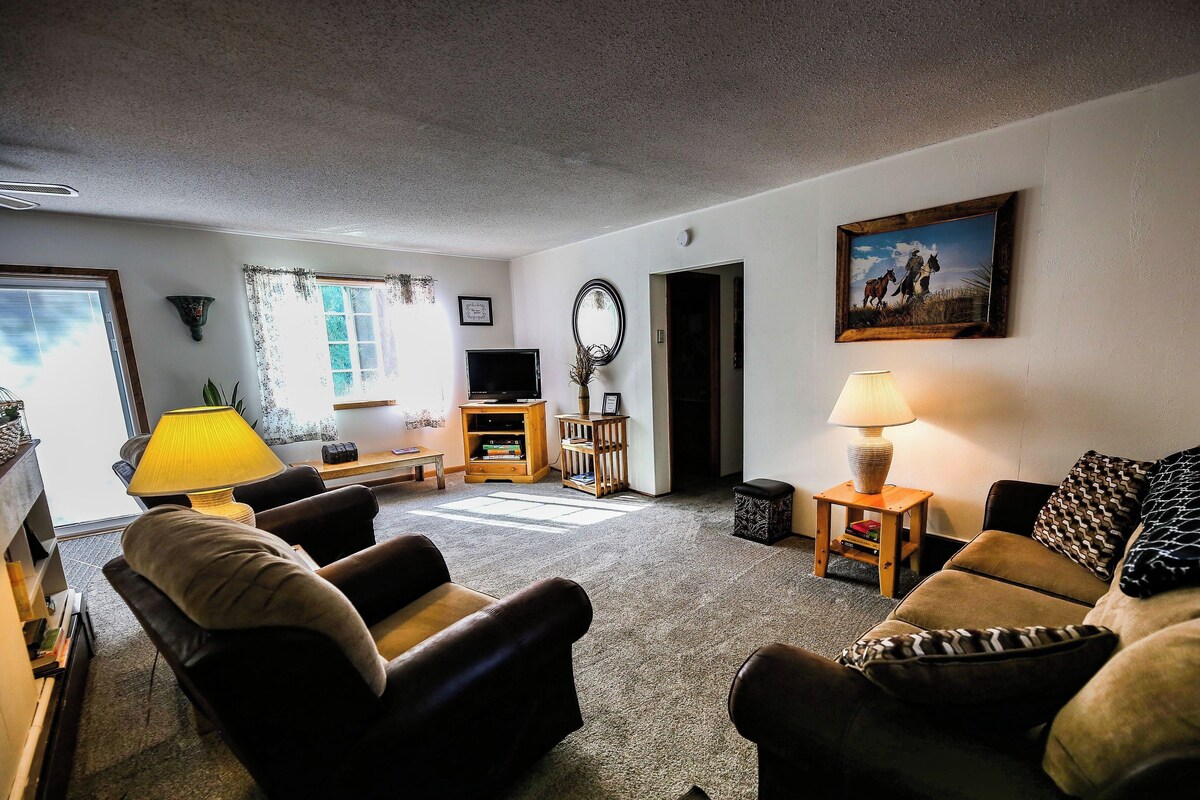 A living room with a sofa, armchairs, a TV, a lamp, and a painting on the wall.
