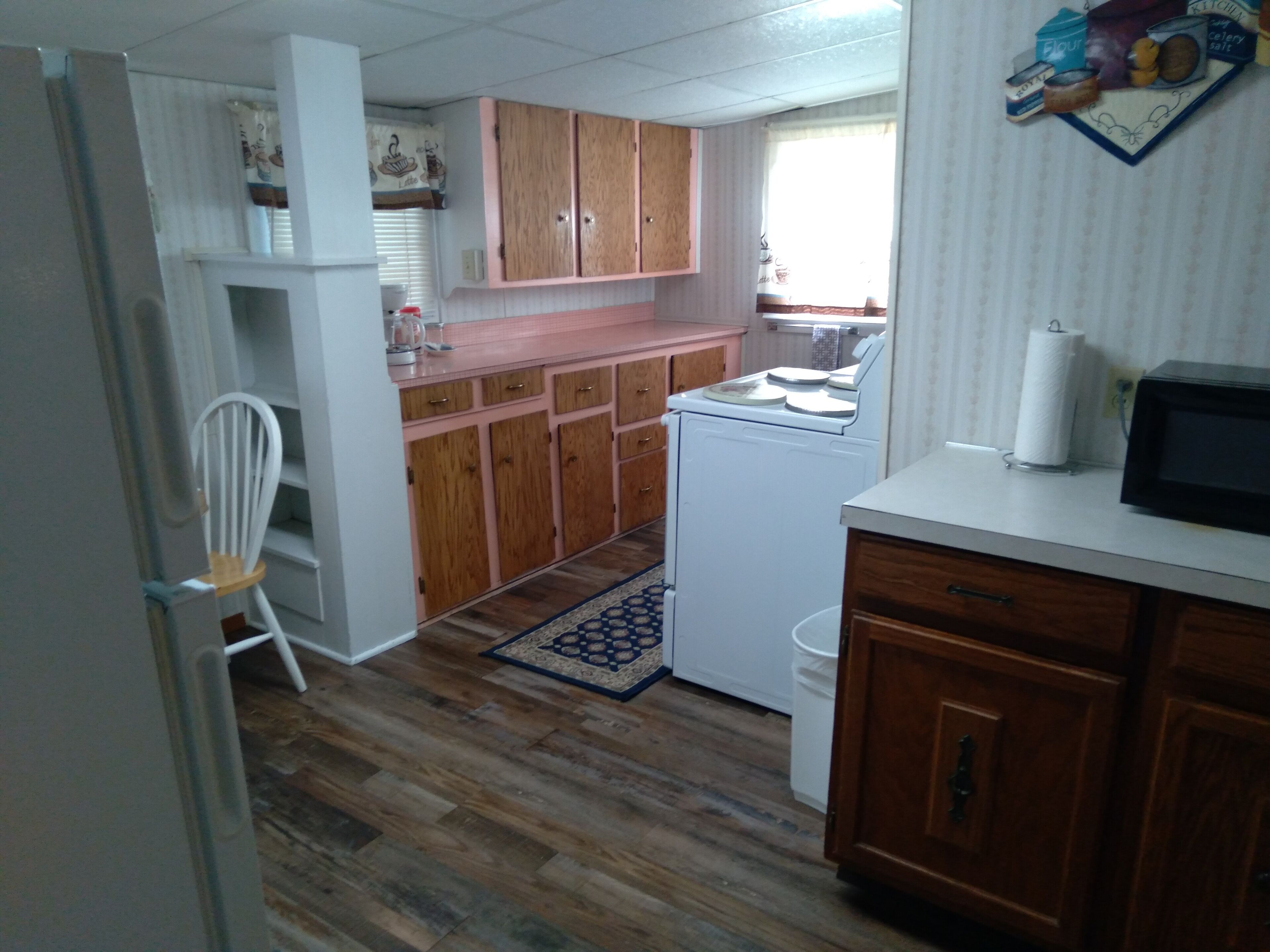 A compact kitchen with wooden cabinets, a white refrigerator, a microwave, and a small sink.