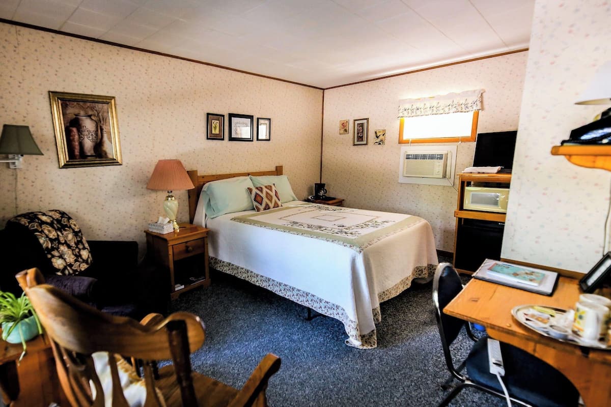 A hotel room with a bed, a desk, a chair, a lamp, a picture frame, and a television.