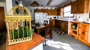 Une cuisine avec des meubles de rangement en bois, une table à manger et une cage à oiseaux jaune ornée de plantes vertes.