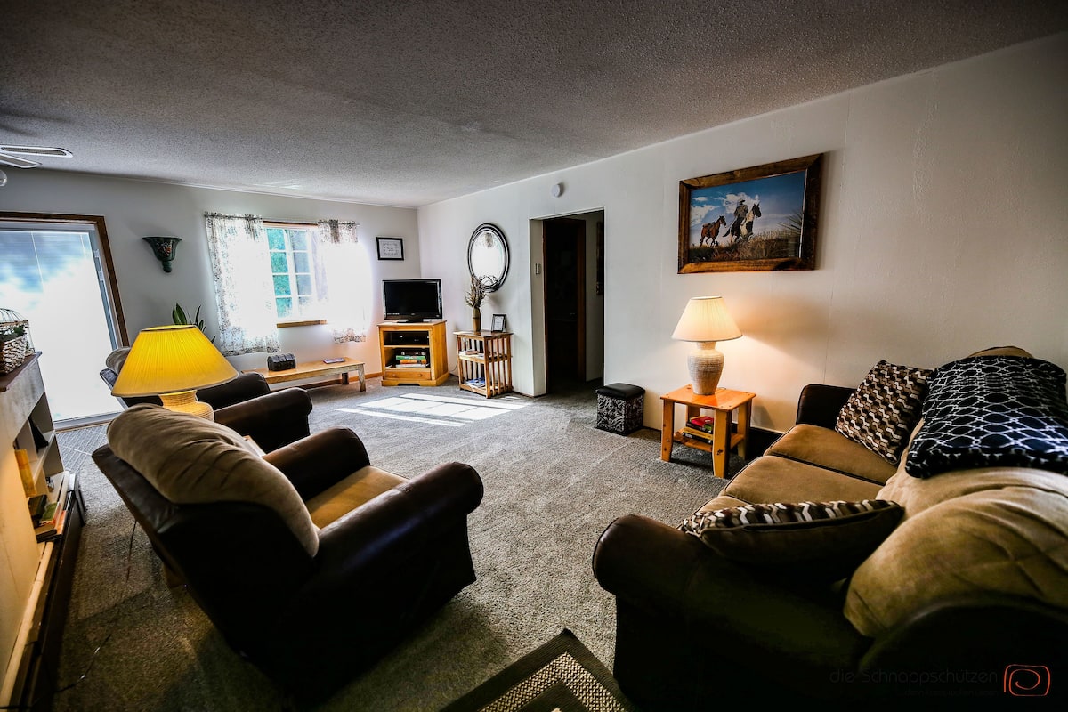 A living room with a sofa, armchairs, a TV, and a lamp.