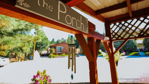 Une pergola en bois, sur laquelle est accroché un panneau indiquant « The Porch », et un carillon éolien qui y est suspendu.