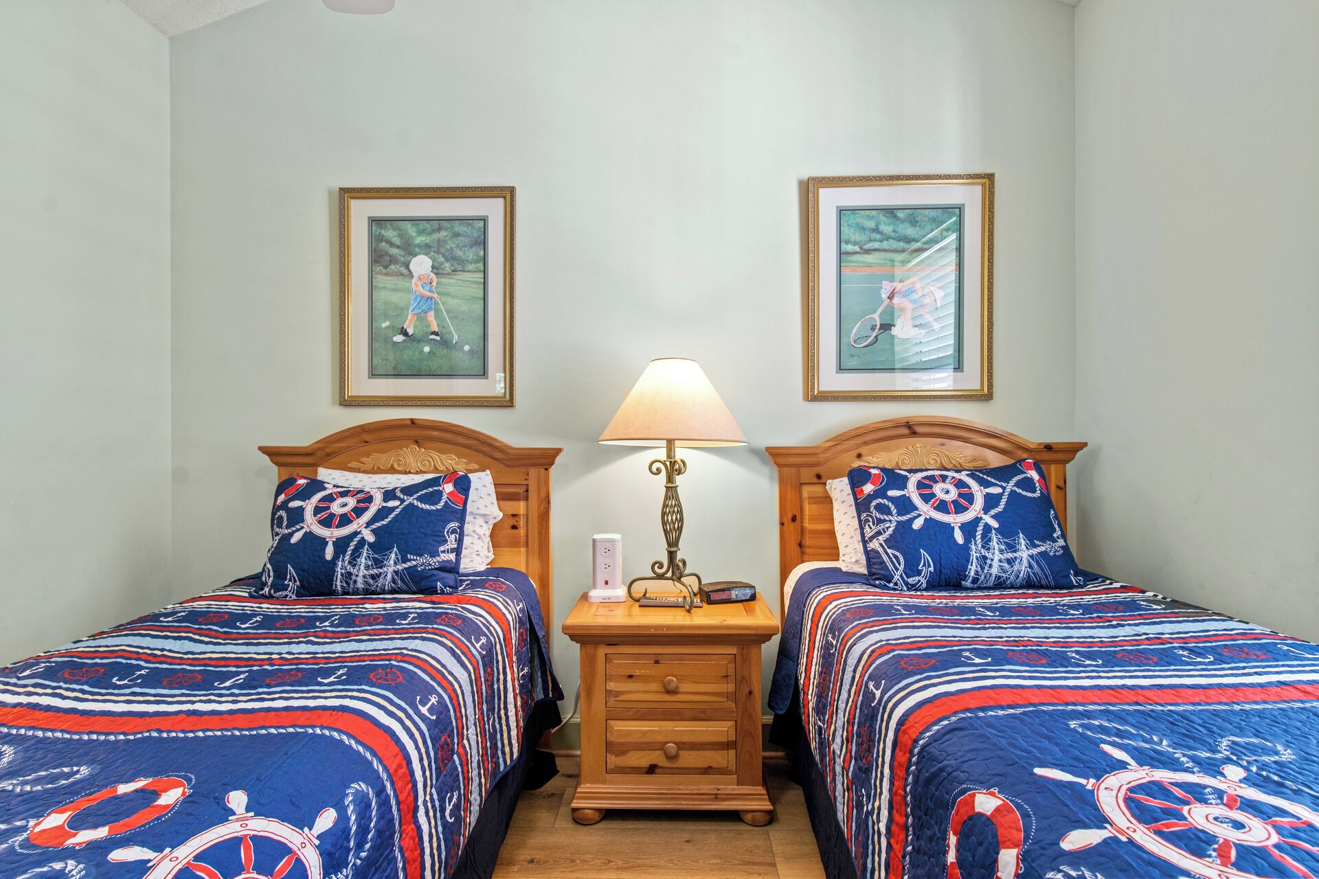 Een slaapkamer met twee bedden, elk met een sprei in nautisch thema, een nachtkastje met een lamp en lijstwerken aan de muren.