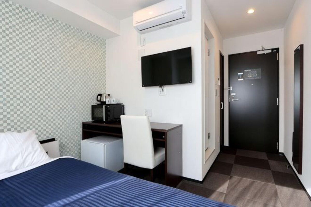A hotel room with a bed, desk, chair, TV, and a door.