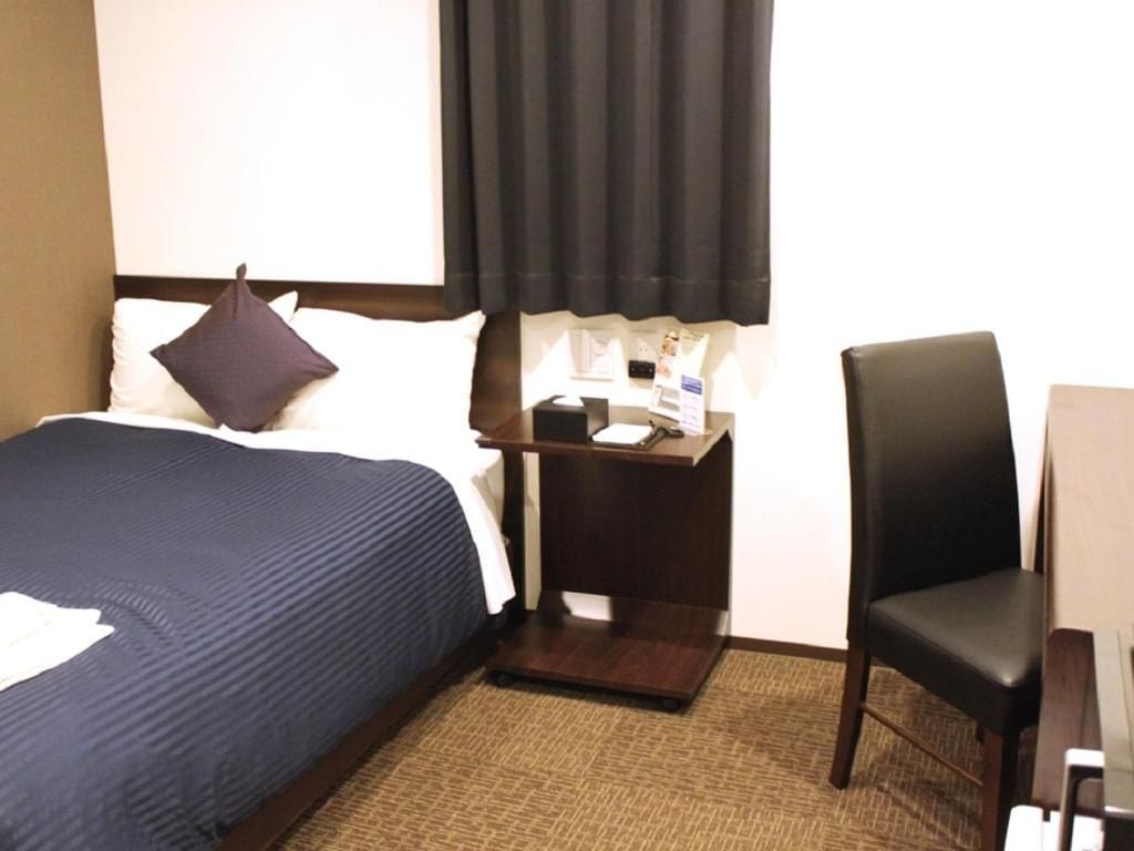 A hotel room with a bed, a chair, a small table, and a nightstand.