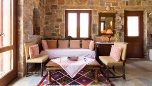 Una habitación con paredes de piedra, una cama, dos sillas, una mesa con camino de mesa y una alfombra estampada.