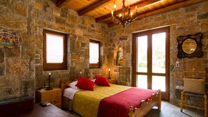 Un dormitorio de paredes de piedra con una cama de madera, almohadas rojas y una araña.