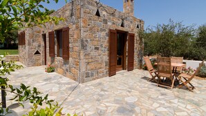 Un edificio de piedra con contraventanas de madera, un patio de piedra y mobiliario de exterior.