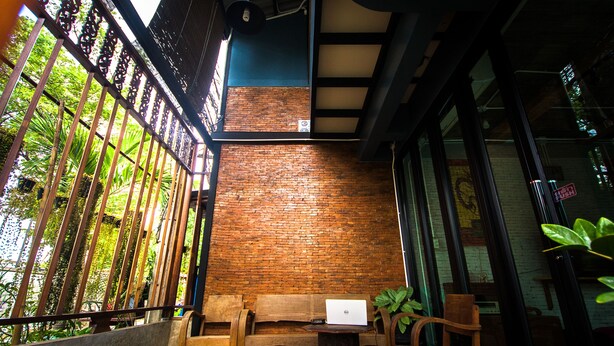 A cozy seating area with a wooden bench and chairs, a laptop on a small table, and a brick wall.