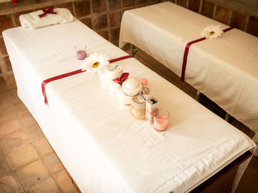Two massage tables with white linens and red ribbons, each with a flower and various spa products.