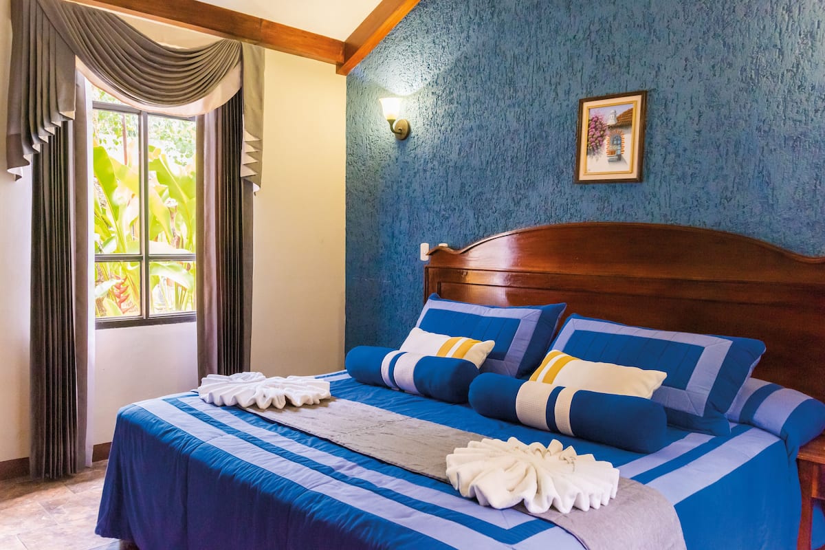 Una cama bien hecha con ropa de cama azul y blanca, un cabecero de madera y una ventana con cortinas.