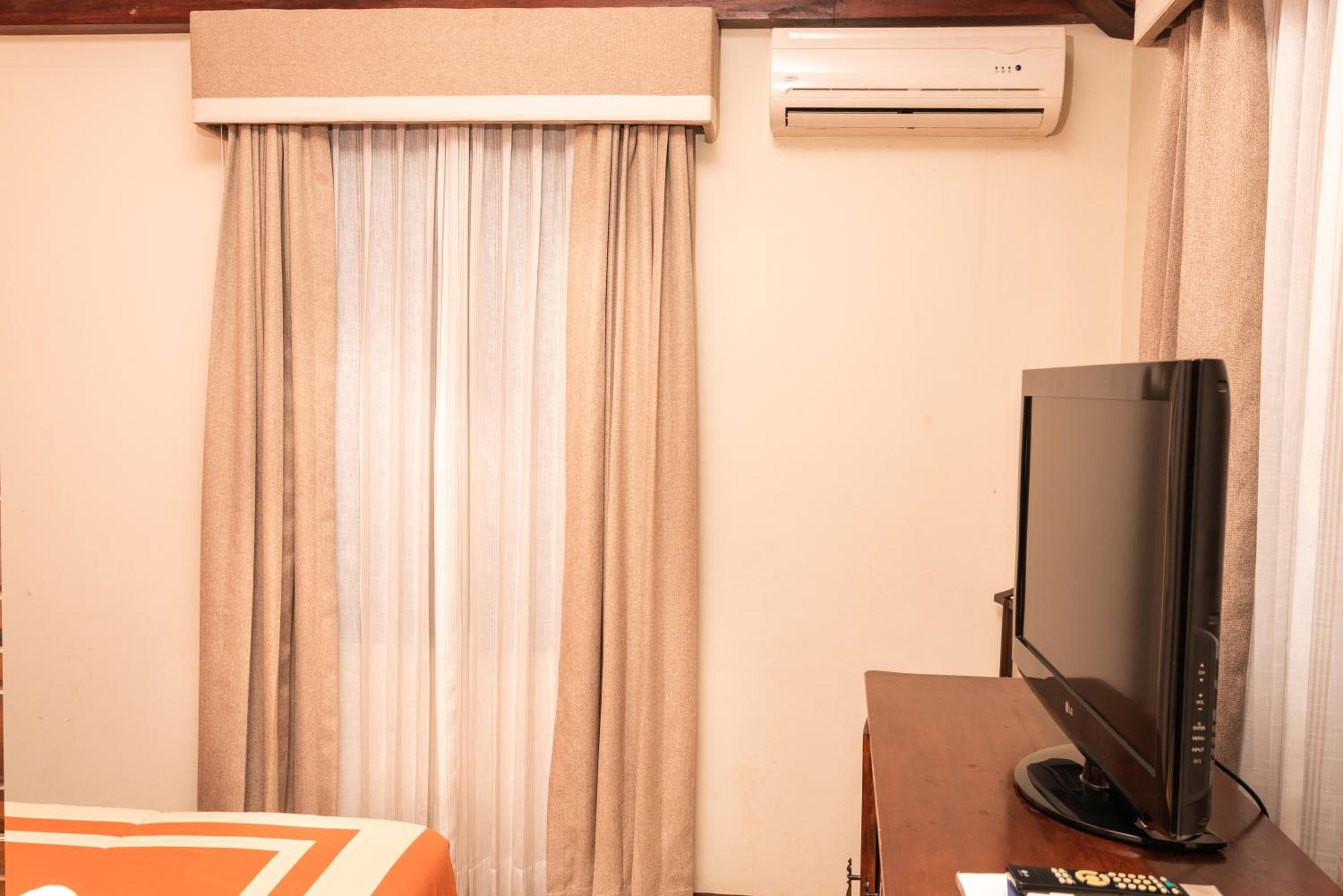 Habitación de hotel con cama, televisor sobre una mesa de madera y aire acondicionado en la pared.