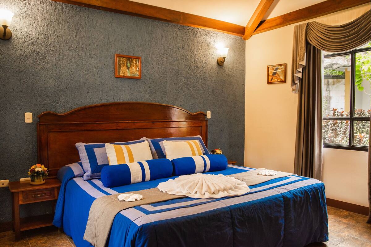 Una cama bien tendida con una colcha azul y blanca a rayas, un cabecero de madera y dos lámparas fijadas a la pared.
