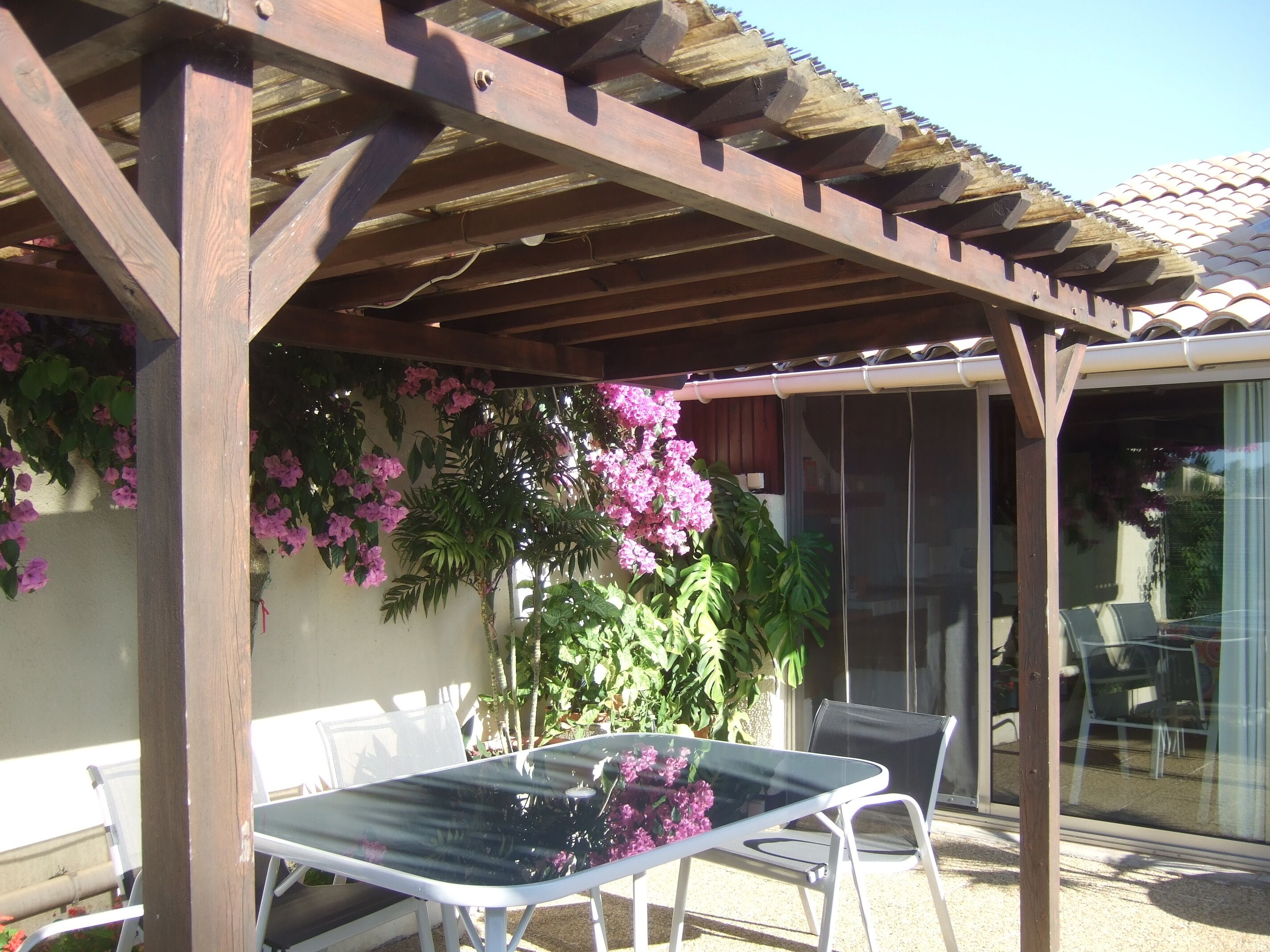 An outdoor patio with a pergola, a glass table, and chairs.