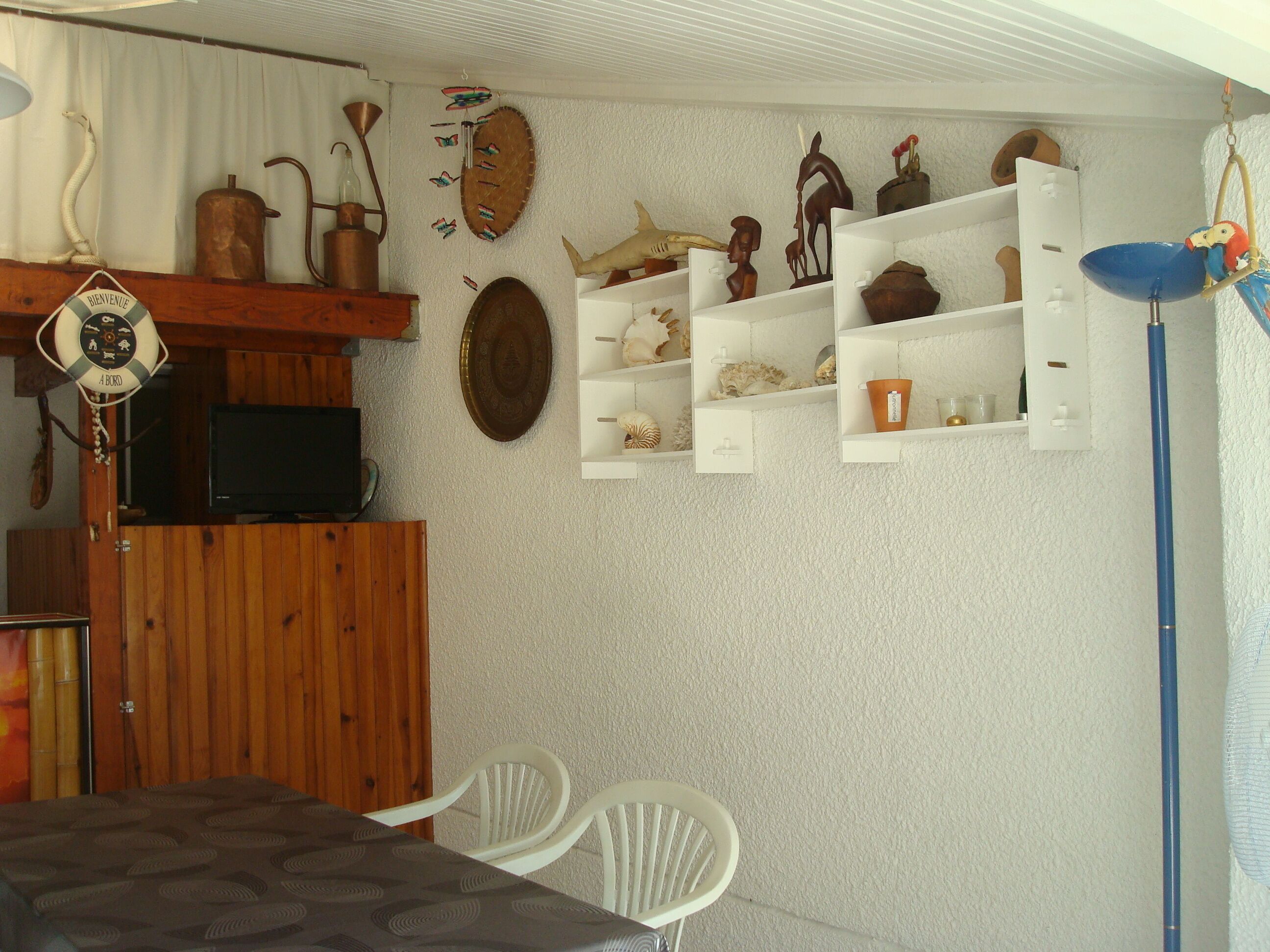 Una stanza con un armadio in legno, una televisione, sedie bianche e mensole con oggetti decorativi.