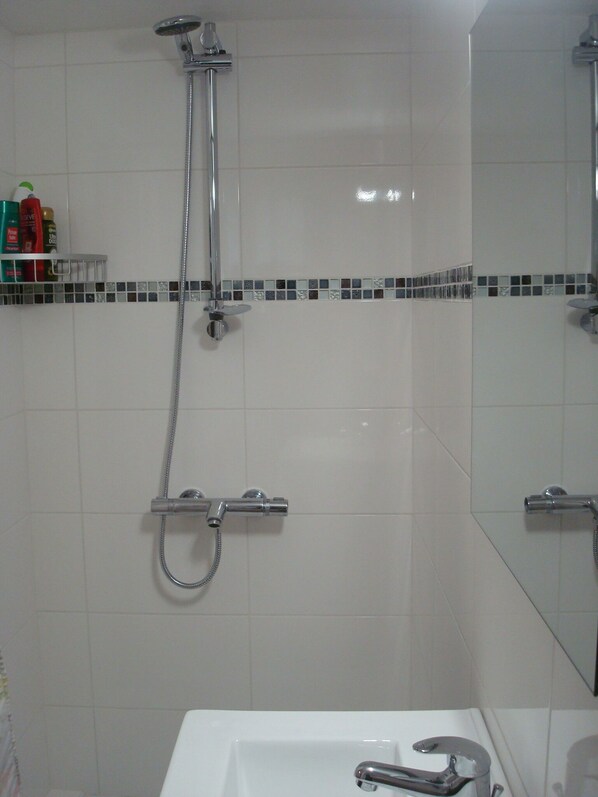 Un baño con ducha, lavamanos y espejo.