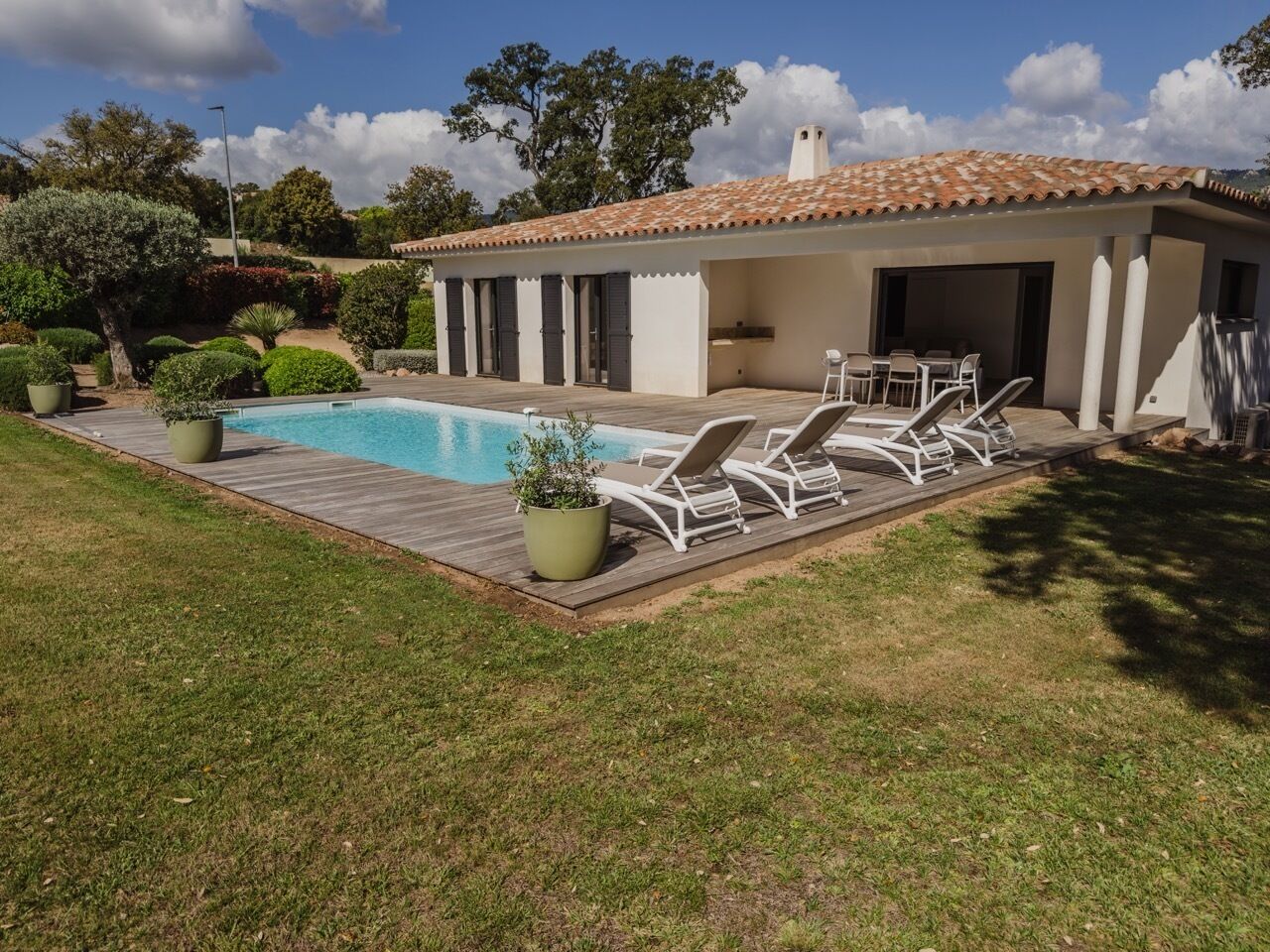 Un área junto a la piscina con tumbonas y un porche cubierto.