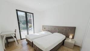 A bedroom with two beds, a desk, and a sliding glass door leading to an outdoor area.