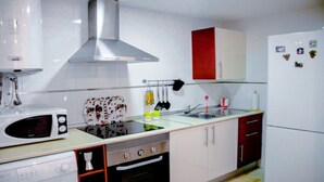 Una cocina con gabinetes blancos, una campana extractora de acero inoxidable, un microondas, una estufa y un refrigerador.