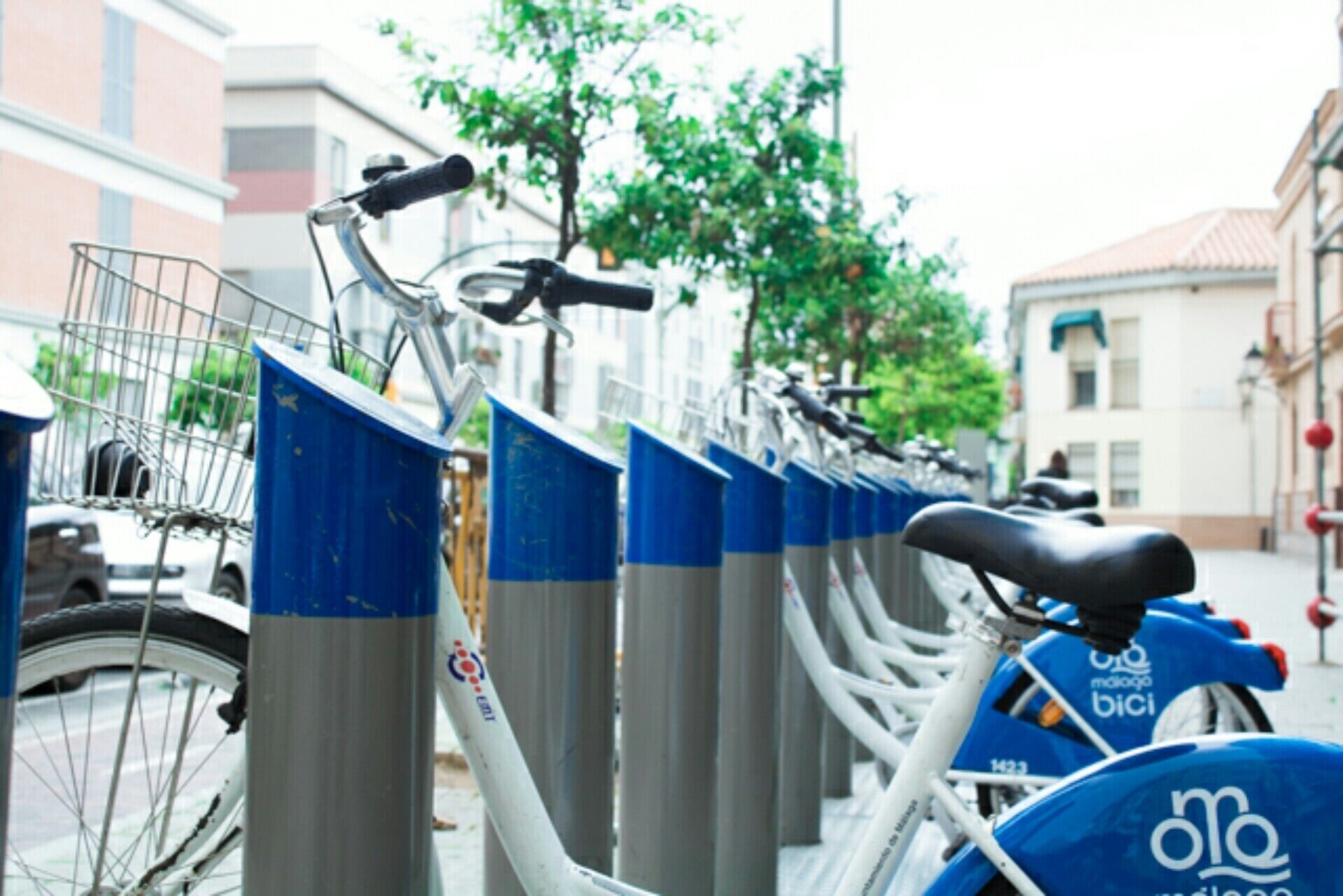 Une rangée de vélos est garée contre un bâtiment, le long d’une clôture en métal.