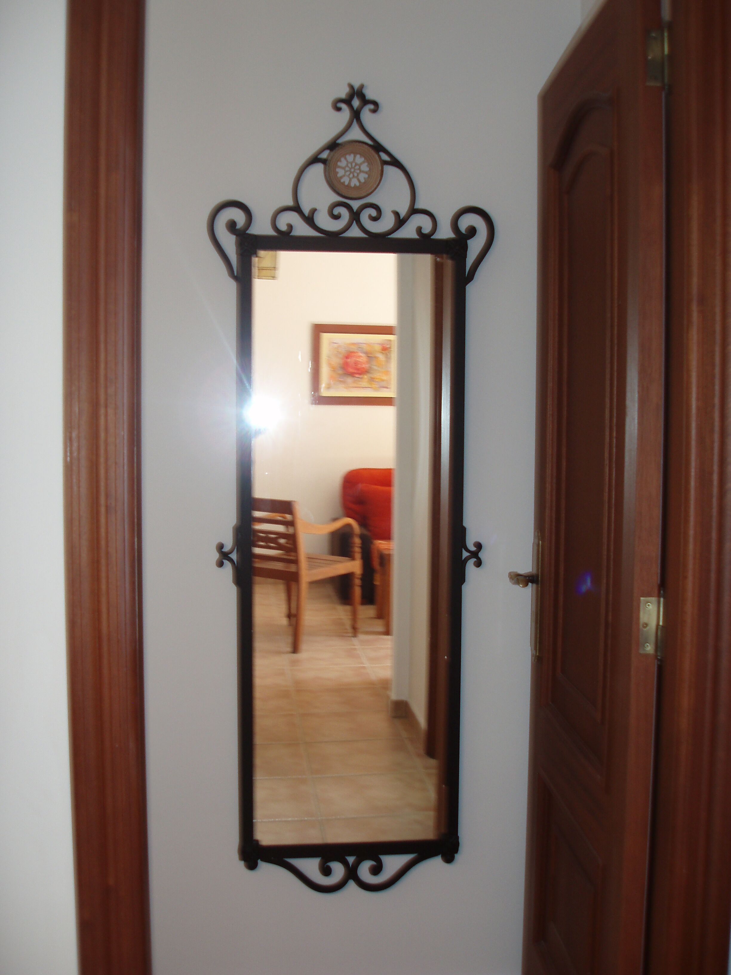 A wooden door with a mirror reflecting a room with a chair and a table.