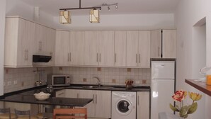 Eine kleine Küche mit Waschmaschine, Mikrowelle und Kühlschrank. Es gibt Barhocker und einen Holzstuhl.