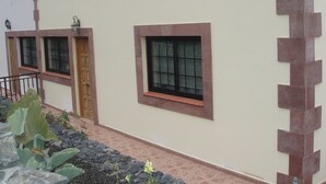 Ein Gebäude mit einer flachen Fassade, zwei Fensterläden, einer Tür und einem kleinen Garten mit Pflanzen und einem Kiesweg.